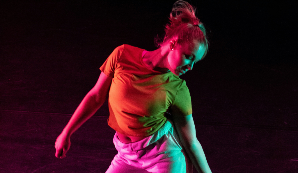 Modern dancer poses in dramatic pink and green stage lighting