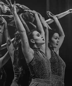 Black and white image of a group of dancers holding a dancer over their heads in a dramatic pose