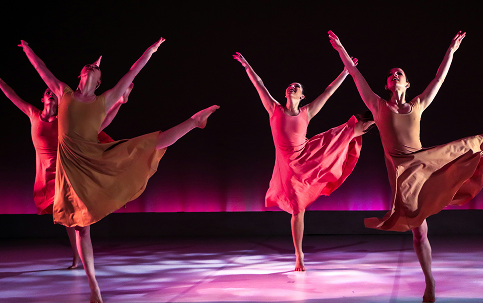 Group of synchronized ballet dancers on stage with dramatic pink lighting
