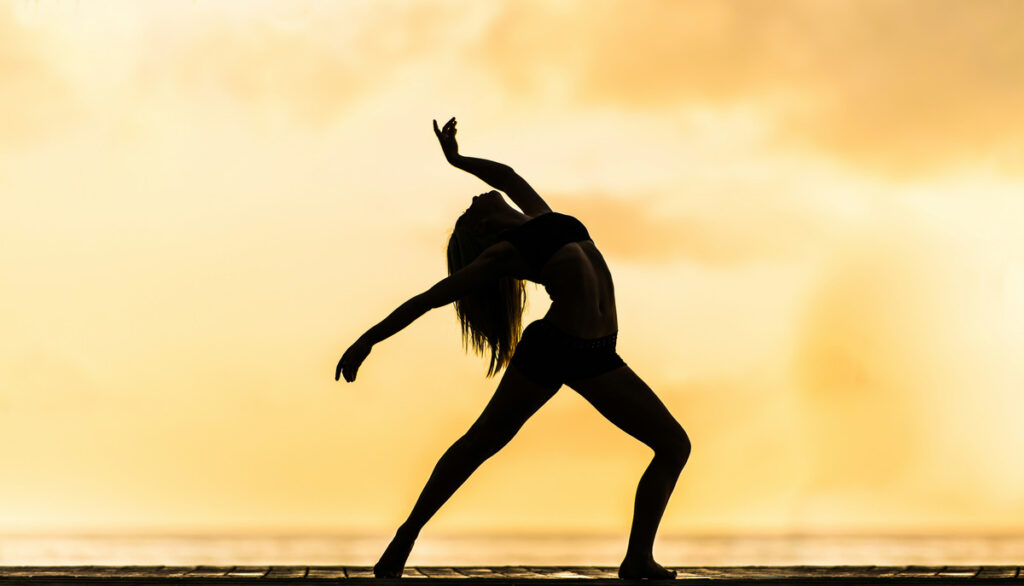 Silhouette of a dancer performing against a golden sunset sky